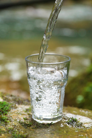 Fresh water pouring into glass on stone near river, closeupの写真素材