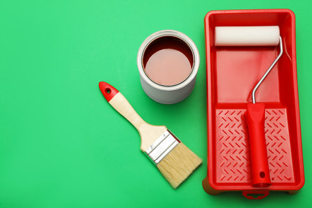 Can of orange paint, brush, roller and container on green background. Space for textの写真素材