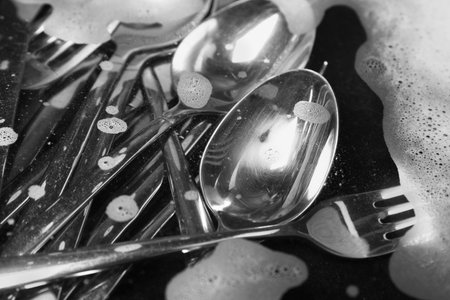 Washing silver spoons, forks and knives in water with foam, closeupの写真素材