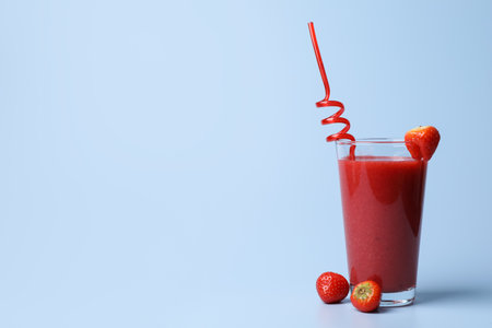 Glass with delicious berry smoothie and fresh strawberries on light blue background. Space for textの写真素材