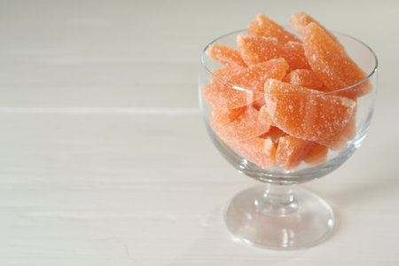 Tasty orange jelly candies in glass dessert bowl on white table. Space for textの写真素材