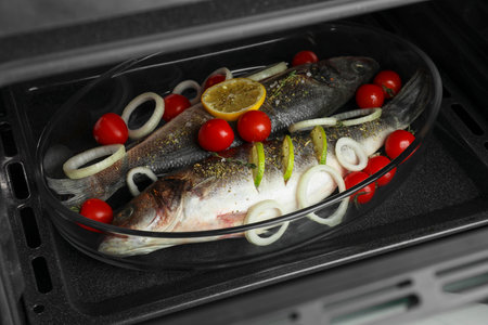 Glass baking tray with raw sea bass fish and ingredients in oven, closeupの写真素材
