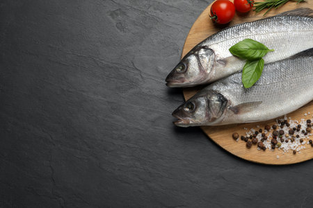 Sea bass fish and ingredients on black table, top view. Space for textの写真素材