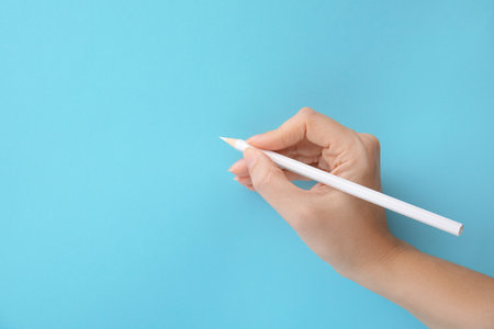Woman with white pencil on light blue background, closeup. Space for textの写真素材