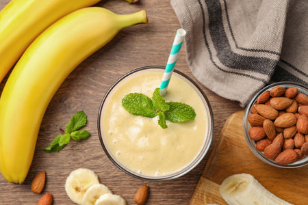 Flat lay composition of banana smoothie in glass and nuts on wooden tableの写真素材