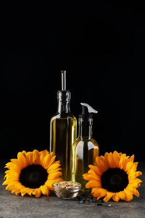 Sunflower cooking oil, seeds and beautiful flowers on gray table against black backgroundの写真素材