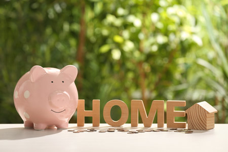 Piggy bank, word Home, house model and coins on table outdoors. saving money conceptの写真素材