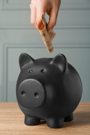 Woman putting banknotes into piggy bank at wooden table, closeupの写真素材