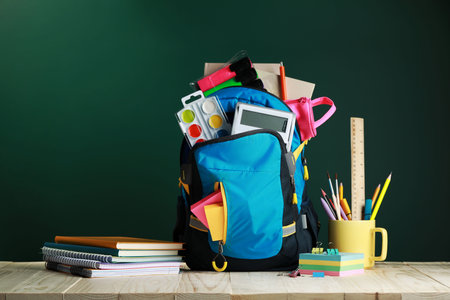 Backpack with different school stationery on white wooden table near chalkboardの写真素材