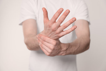 Man suffering from pain in his hand on light background, closeup. arthritis symptomsの写真素材