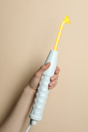 Woman holding working high frequency darsonval device on beige background, closeupの写真素材