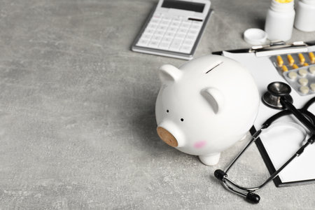 Piggy bank, stethoscope, calculator, clipboard and pills on light grey table, space for text. Medical insuranceの写真素材