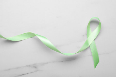 World Mental Health Day. Green ribbon on white marble table, top viewの写真素材