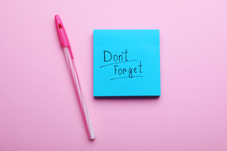 Paper note with phrase Don't Forget and pen on pink background, flat layの写真素材