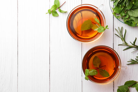 Cups of aromatic herbal tea with mint and rosemary on white wooden table, flat lay. Space for textの写真素材
