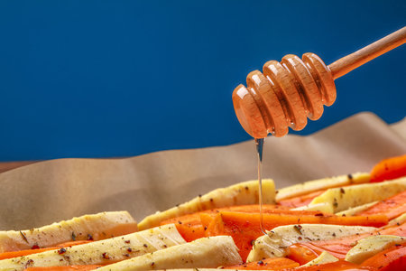 Pouring honey onto slices of parsnip and carrot against blue background, closeupの写真素材