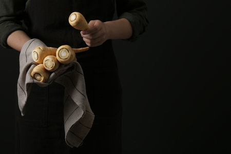 Woman holding fresh ripe parsnips on black background, closeup. Space for text