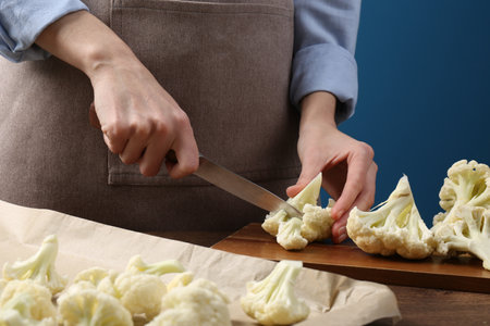 Woman cutting fresh cauliflower at wooden table, closeupの写真素材