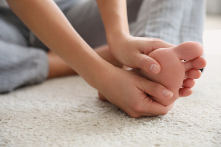 Young woman suffering from pain in foot on floor, closeupの写真素材