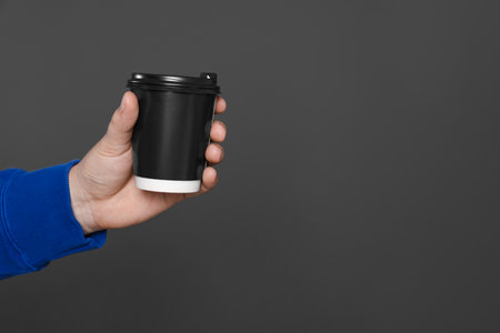 Man holding takeaway cup with drink on dark grey background, closeup view and space for text. Coffee to goの写真素材