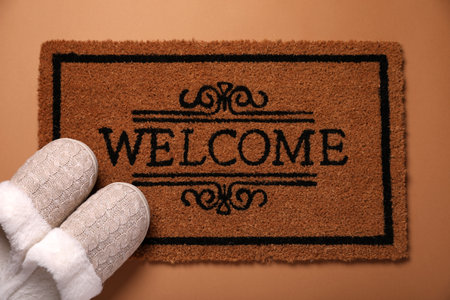Doormat with word Welcome and slippers on brown background, flat layの写真素材