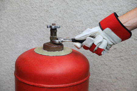 Worker with adjustable wrench opening red gas cylinder near wall, closeup