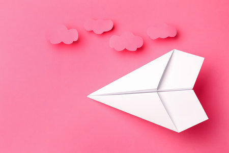 Handmade white paper plane with clouds on pink background, flat lay. Space for textの写真素材
