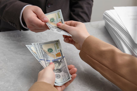 Woman giving money to man at light grey table, closeup. Currency exchange