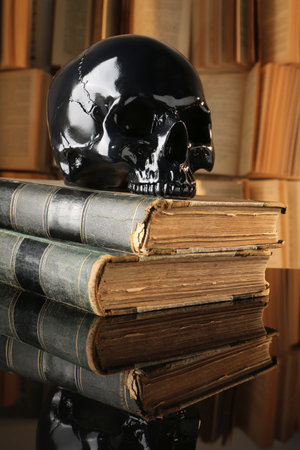 Black human skull and old books on mirror tableの写真素材
