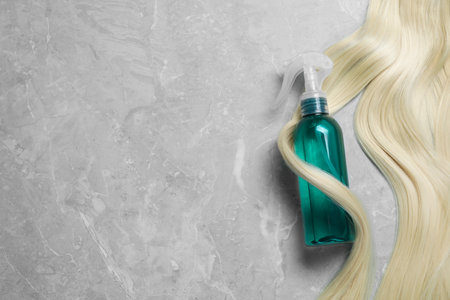 Spray bottle with thermal protection and lock of blonde hair on grey marble table, flat lay. Space for textの写真素材