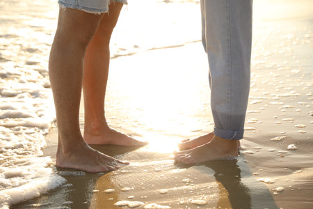 Couple on sandy beach near sea at sunset, closeup of legsの写真素材