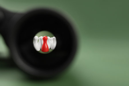 Recruiter searching employee. Red and white pawns visible through binoculars on green background. Space for textの写真素材