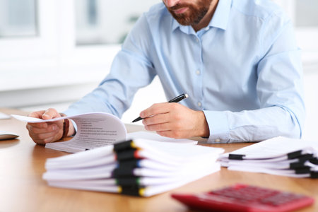 Man working with documents at wooden table in office, closeup
