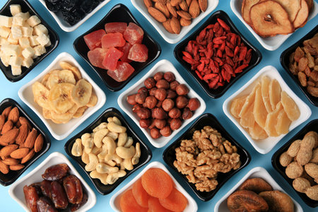 Bowls with dried fruits and nuts on light blue background, flat layの写真素材
