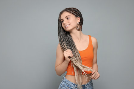 Beautiful woman with long african braids on gray background, space for text