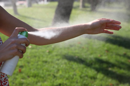 Woman applying insect repellent onto hand in park, closeup