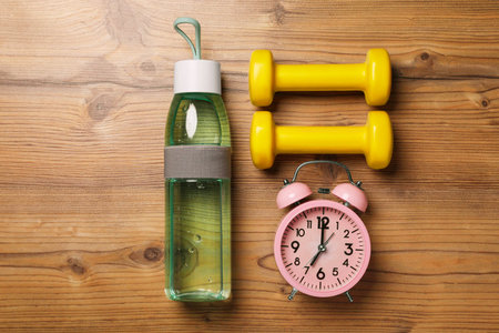 Alarm clock, dumbbells and bottle of water on wooden table, flat lay. Morning exerciseの写真素材