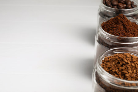 Jars with instant, ground coffee and roasted beans on white table, space for textの写真素材