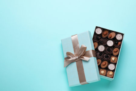 Open box of delicious chocolate candies on light blue background, flat lay. Space for textの写真素材