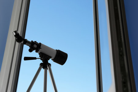 Tripod with modern telescope near open window indoors, low angle view. Space for textの写真素材