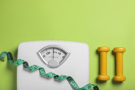 weight loss concept. Scales, dumbbells and measuring tape on green background, flat lay. Space for textの写真素材