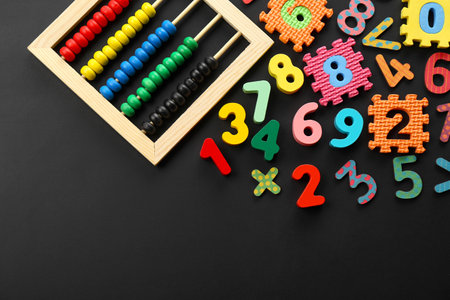 Many colorful numbers and mathematical symbols near abacus on black background, flat lay. Space for textの写真素材