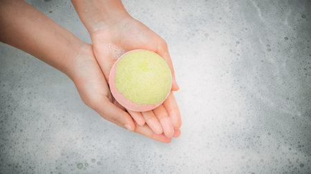 Woman holding bath bomb over water with foam, top view. Space for textの写真素材