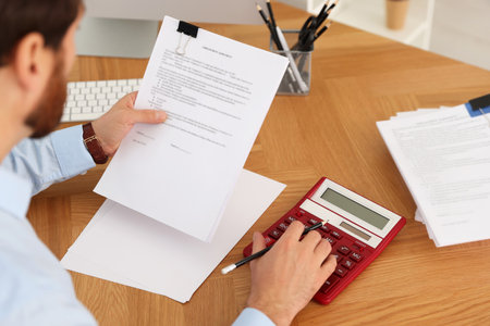 Man working with documents and using calculator at wooden table in office, above viewの写真素材