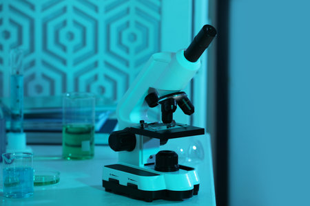 Modern microscope with glass slide on white table in laboratory, toned in blue