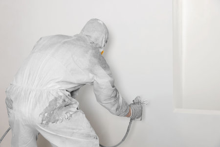 Decorator in protective overalls painting wall with spray gun indoorsの写真素材