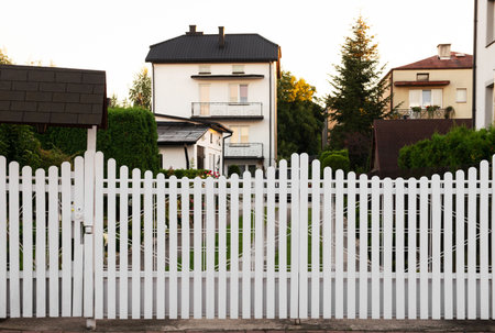 Houses and trees behind white wooden fence outdoorsの写真素材