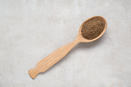 Spoon of celery seeds on light gray textured table, top view
