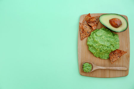 Delicious guacamole made of avocados, nachos and cut fruit on color background, top view. Space for...