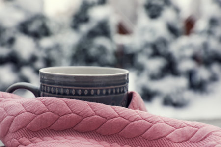Winter morning. Cup with hot drink wrapped in pink sweater outdoors, closeup. Space for textの写真素材